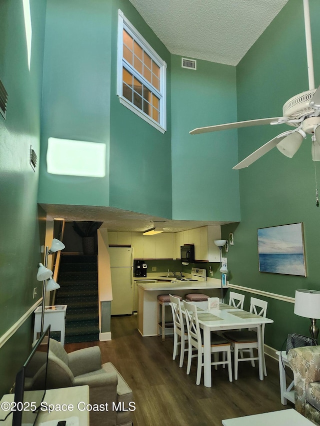 kitchen featuring ceiling fan, dark hardwood / wood-style flooring, a high ceiling, white appliances, and a textured ceiling