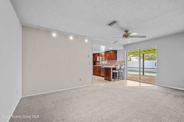 unfurnished living room with ceiling fan, a textured ceiling, and light carpet