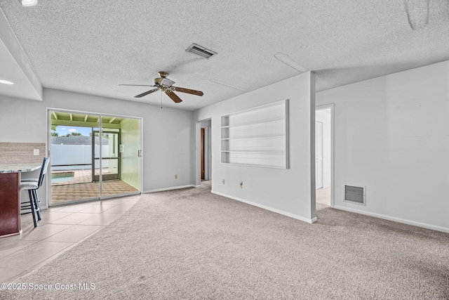 unfurnished living room with light carpet, ceiling fan, a textured ceiling, and built in shelves