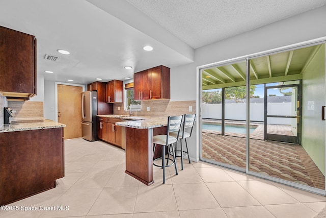 kitchen featuring kitchen peninsula, decorative backsplash, light stone countertops, a breakfast bar area, and stainless steel fridge