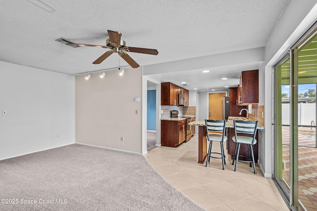 kitchen with stainless steel appliances, a kitchen breakfast bar, track lighting, light colored carpet, and a textured ceiling