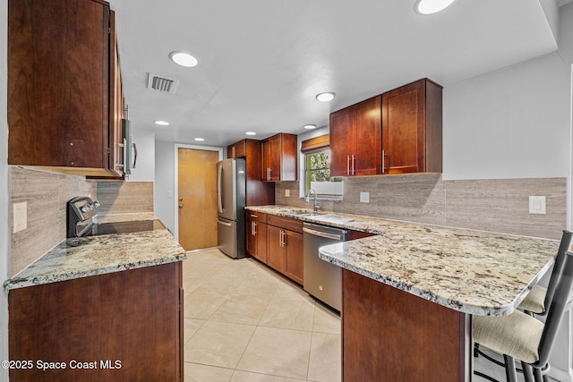 kitchen with appliances with stainless steel finishes, a kitchen bar, kitchen peninsula, and light stone counters