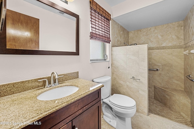 bathroom with tiled shower, vanity, and toilet