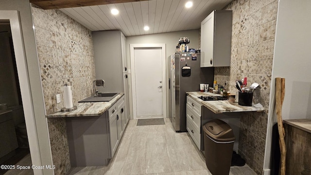 kitchen with wooden ceiling, backsplash, light stone countertops, white cabinets, and sink