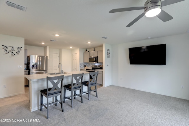 kitchen with sink, appliances with stainless steel finishes, a kitchen breakfast bar, an island with sink, and light carpet