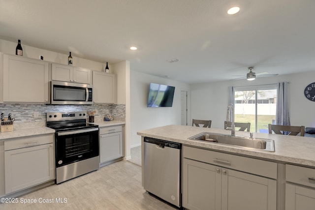 kitchen featuring appliances with stainless steel finishes, tasteful backsplash, white cabinets, light hardwood / wood-style flooring, and sink