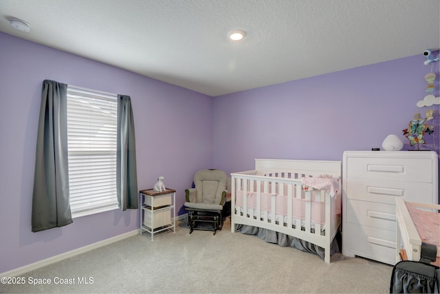 carpeted bedroom featuring a nursery area and a textured ceiling