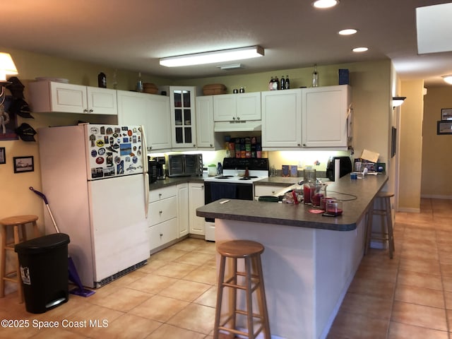 kitchen featuring range with electric stovetop, a kitchen breakfast bar, kitchen peninsula, and white fridge