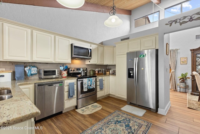 kitchen featuring tasteful backsplash, hanging light fixtures, appliances with stainless steel finishes, light stone counters, and cream cabinets