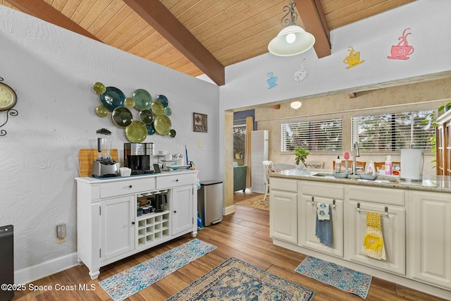 kitchen featuring pendant lighting, white cabinetry, vaulted ceiling with beams, sink, and light wood-type flooring