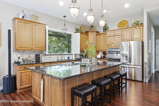 kitchen with a kitchen island, dark stone countertops, appliances with stainless steel finishes, and pendant lighting