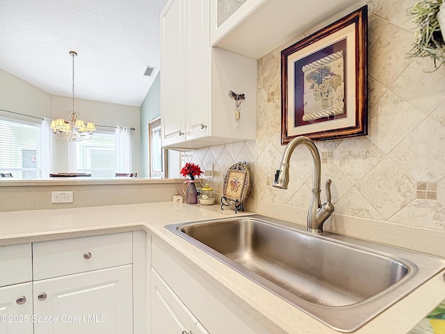 kitchen featuring sink, decorative backsplash, a textured ceiling, white cabinets, and decorative light fixtures