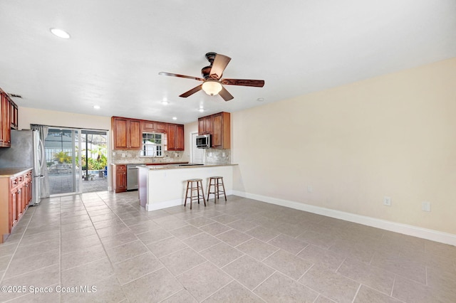 kitchen featuring ceiling fan, appliances with stainless steel finishes, a kitchen breakfast bar, decorative backsplash, and kitchen peninsula