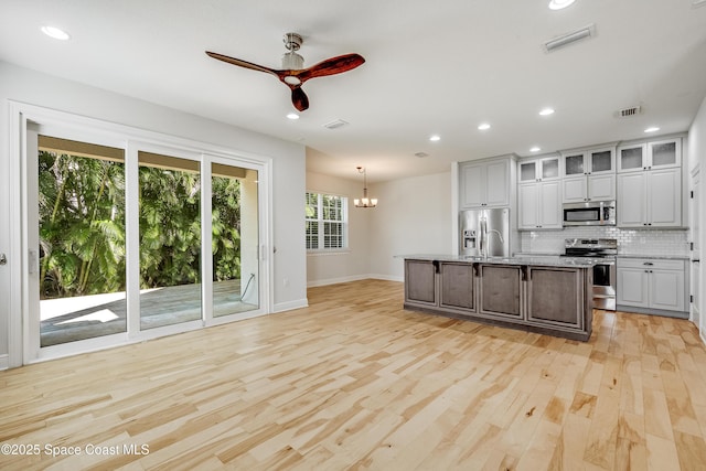 kitchen featuring gray cabinets, appliances with stainless steel finishes, hanging light fixtures, a center island with sink, and decorative backsplash