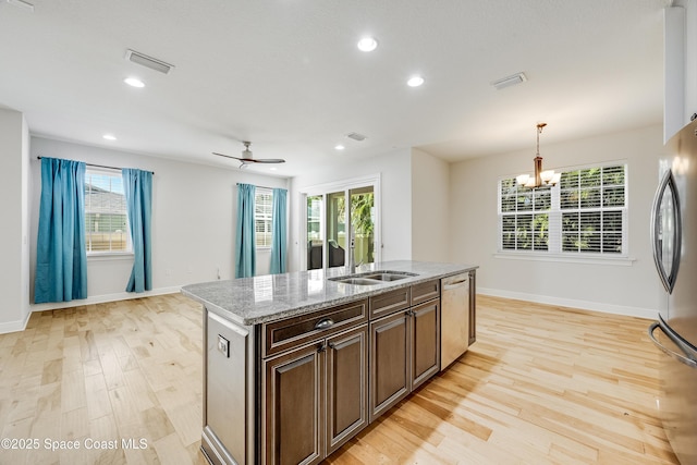 kitchen featuring pendant lighting, sink, stainless steel appliances, light stone countertops, and a center island with sink