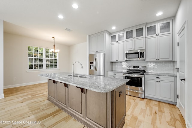 kitchen featuring sink, white cabinetry, a center island with sink, stainless steel appliances, and light stone countertops