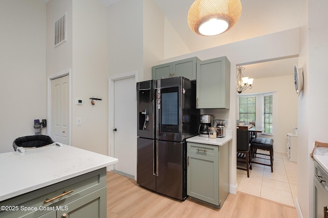 kitchen with an inviting chandelier, high vaulted ceiling, light wood-type flooring, stainless steel refrigerator, and pendant lighting