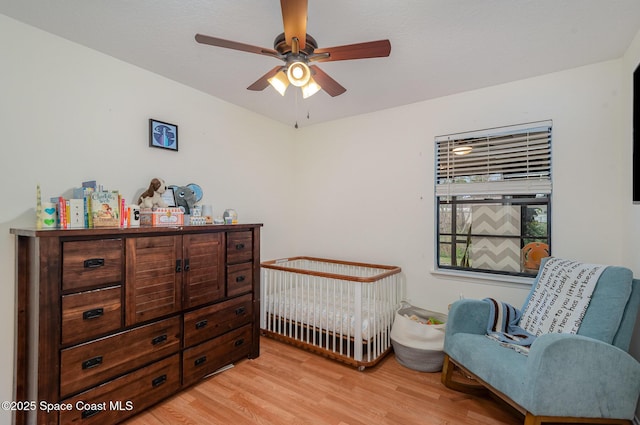 bedroom featuring a nursery area, light wood-type flooring, and ceiling fan