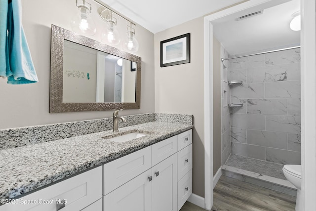 bathroom with tiled shower, vanity, toilet, and wood-type flooring