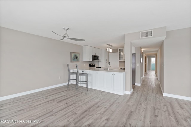 kitchen with appliances with stainless steel finishes, kitchen peninsula, light wood-type flooring, and white cabinets