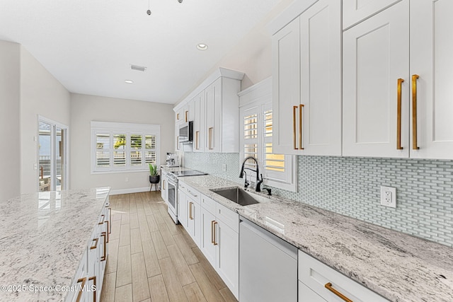 kitchen with dishwashing machine, electric range, sink, white cabinets, and light stone counters