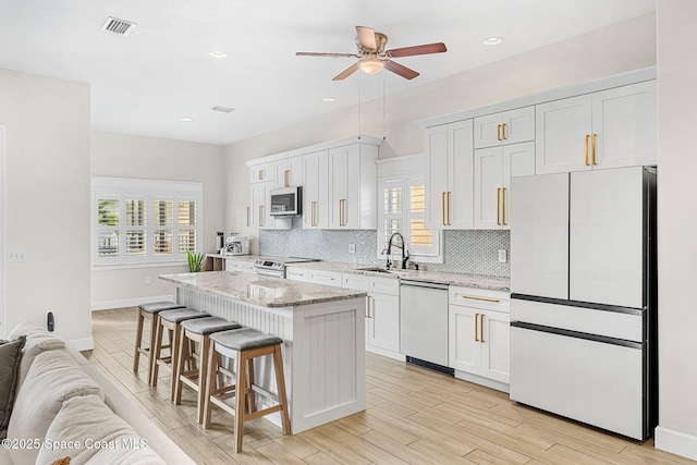 kitchen with light stone countertops, a center island, white cabinetry, stainless steel appliances, and sink