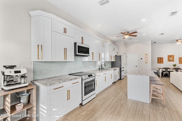 kitchen featuring ceiling fan, a kitchen island, white cabinetry, light stone countertops, and stainless steel appliances