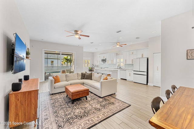 living room featuring a textured ceiling, ceiling fan, light hardwood / wood-style flooring, and sink