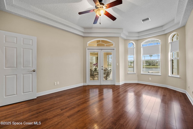 empty room featuring a tray ceiling, dark wood-type flooring, french doors, and a textured ceiling