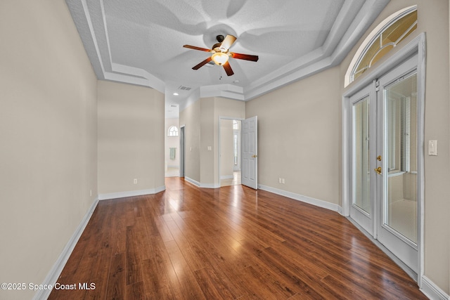 unfurnished room featuring ceiling fan, a tray ceiling, dark hardwood / wood-style flooring, and a textured ceiling