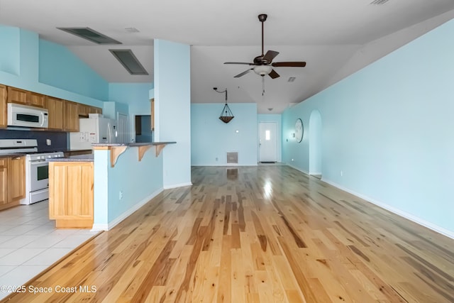 kitchen with white appliances, a breakfast bar area, ceiling fan, light hardwood / wood-style floors, and kitchen peninsula