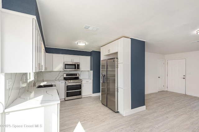 kitchen featuring white cabinetry, stainless steel appliances, decorative backsplash, light stone counters, and sink