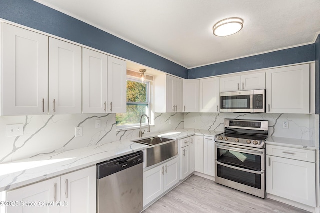 kitchen with sink, light hardwood / wood-style flooring, light stone countertops, appliances with stainless steel finishes, and white cabinets