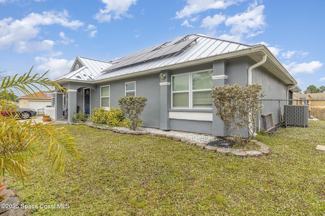 view of front of property with central AC unit, solar panels, and a front lawn