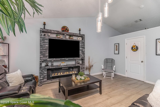 living room with light wood-type flooring, a stone fireplace, a textured ceiling, and lofted ceiling