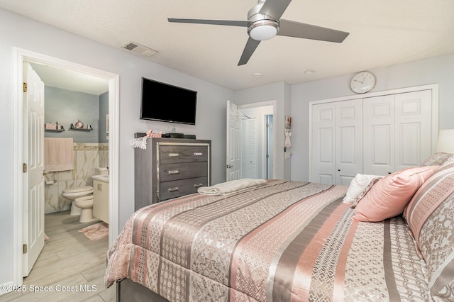 bedroom with ensuite bath, light hardwood / wood-style floors, tile walls, a closet, and ceiling fan