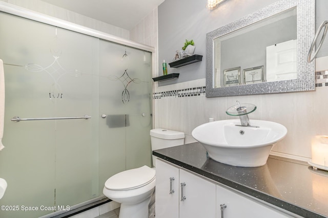 bathroom with a shower with shower door, tile walls, toilet, and vanity