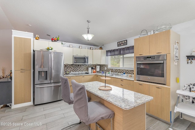 kitchen with hanging light fixtures, appliances with stainless steel finishes, light stone countertops, a kitchen island, and a breakfast bar area