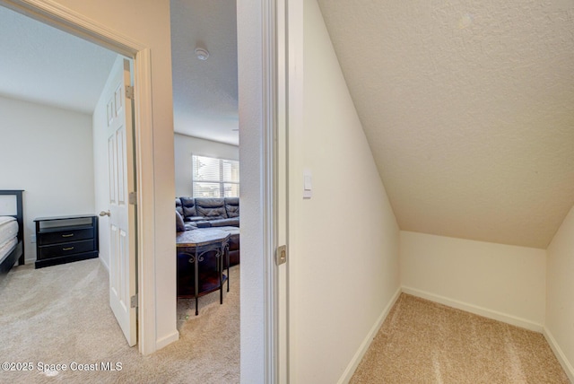 corridor featuring vaulted ceiling, light colored carpet, and a textured ceiling