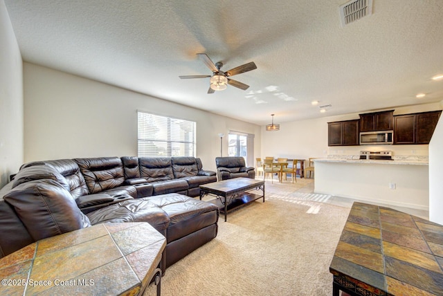 carpeted living room featuring ceiling fan and a textured ceiling