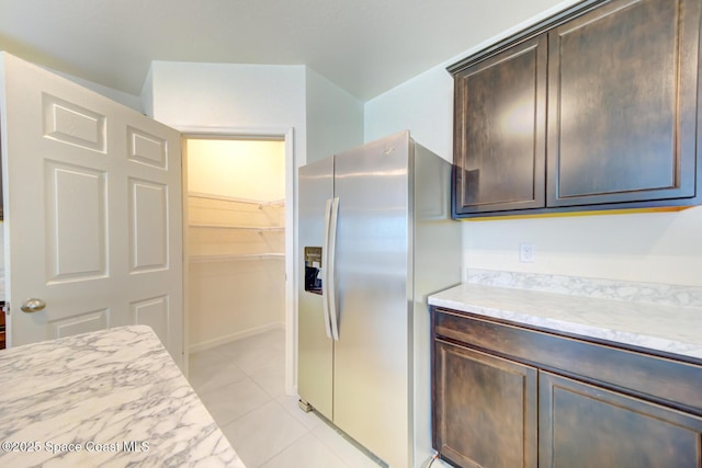 kitchen featuring stainless steel refrigerator with ice dispenser, light stone countertops, dark brown cabinets, and light tile patterned flooring