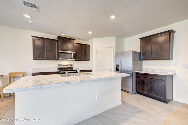 kitchen with a kitchen island with sink, sink, dark brown cabinets, and appliances with stainless steel finishes