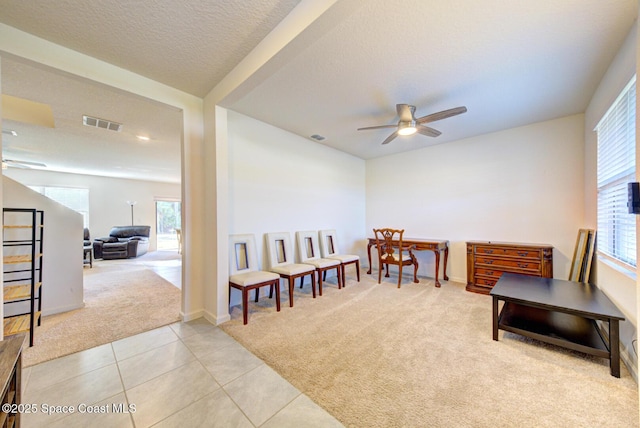 living area with ceiling fan, light carpet, and a textured ceiling