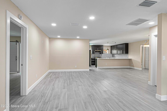 unfurnished living room with a barn door, sink, and light hardwood / wood-style flooring