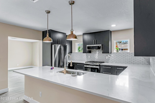 kitchen featuring stainless steel appliances, sink, kitchen peninsula, and decorative light fixtures