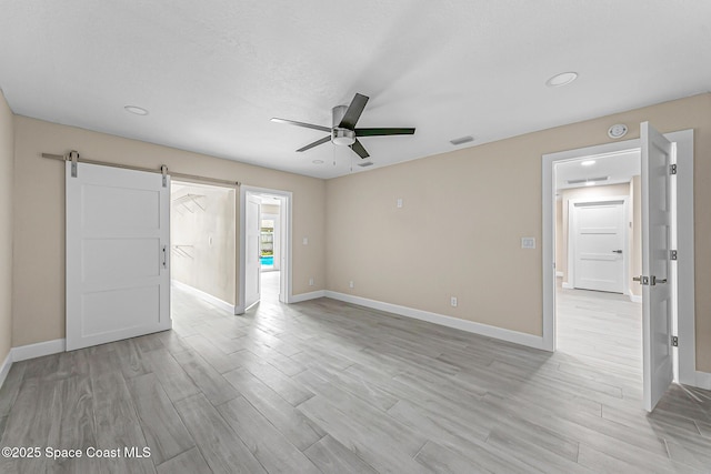 unfurnished room featuring a barn door, ceiling fan, and light wood-type flooring