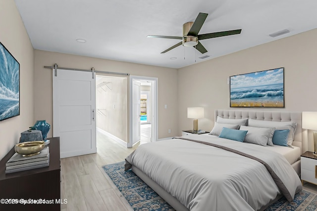 bedroom featuring ceiling fan, a barn door, and light wood-type flooring