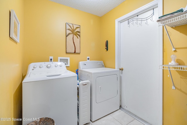 washroom featuring a textured ceiling, light tile patterned floors, and washing machine and clothes dryer