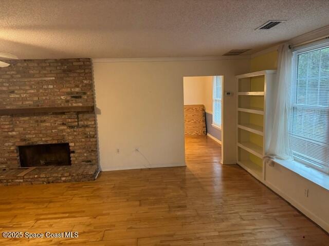 unfurnished living room featuring a textured ceiling, light hardwood / wood-style flooring, a brick fireplace, and ornamental molding