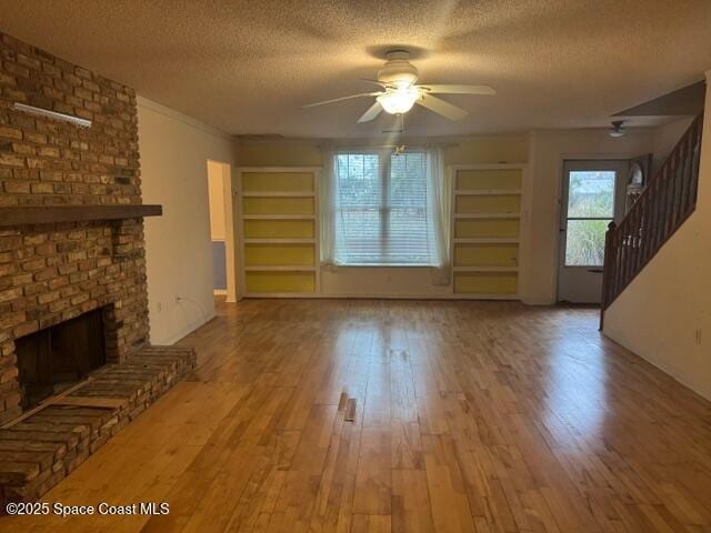 unfurnished living room featuring ceiling fan, light wood-type flooring, a textured ceiling, and a brick fireplace